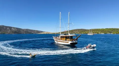 Aborda yacht sailing near rocky coastline at sunset with blue sea