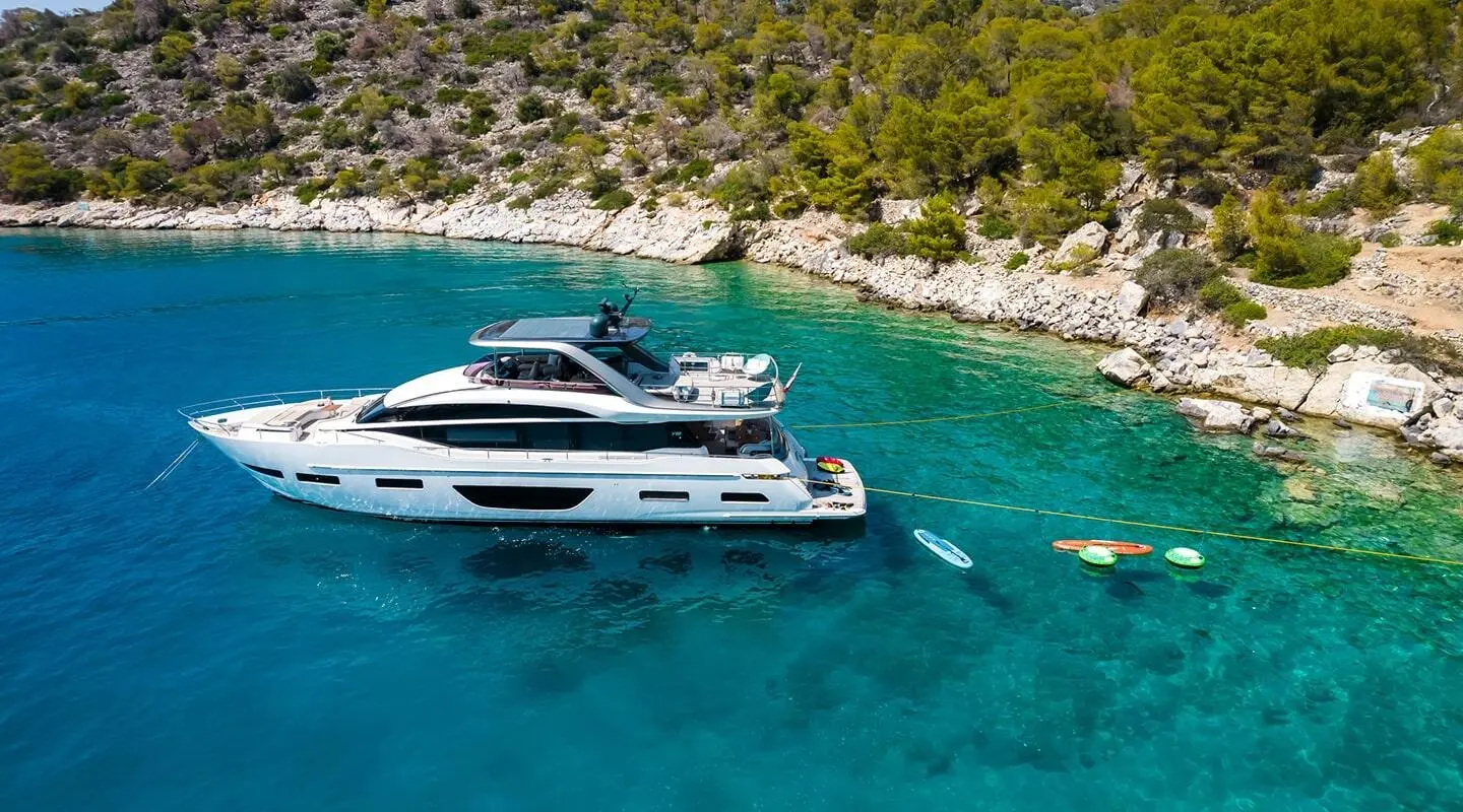 Yacht Vista moored near rocky shoreline with clear blue sea and wood deck