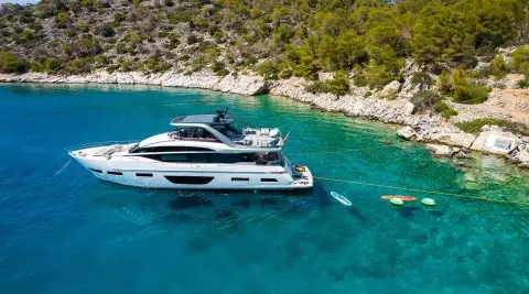 Yacht Vista moored near rocky shoreline with clear blue sea and wood deck