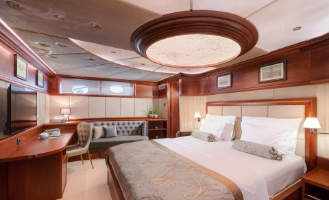 Bedroom aboard a luxury yacht with a large bed, upholstered headboard, and wooden panels with lamps