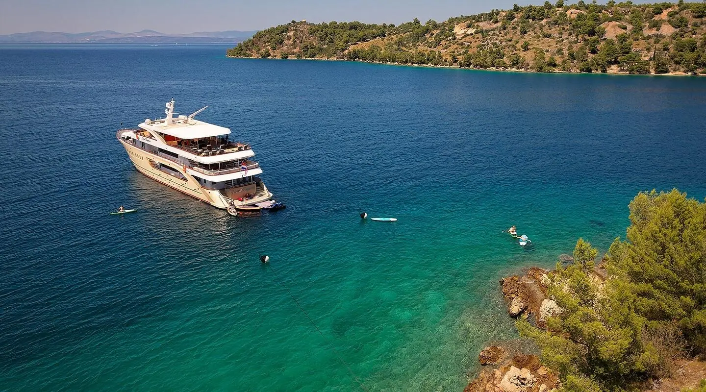 Queen Eleganza yacht anchored near rocky coast at sunset harbor