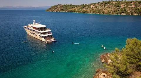 Queen Eleganza yacht anchored near rocky coast at sunset harbor