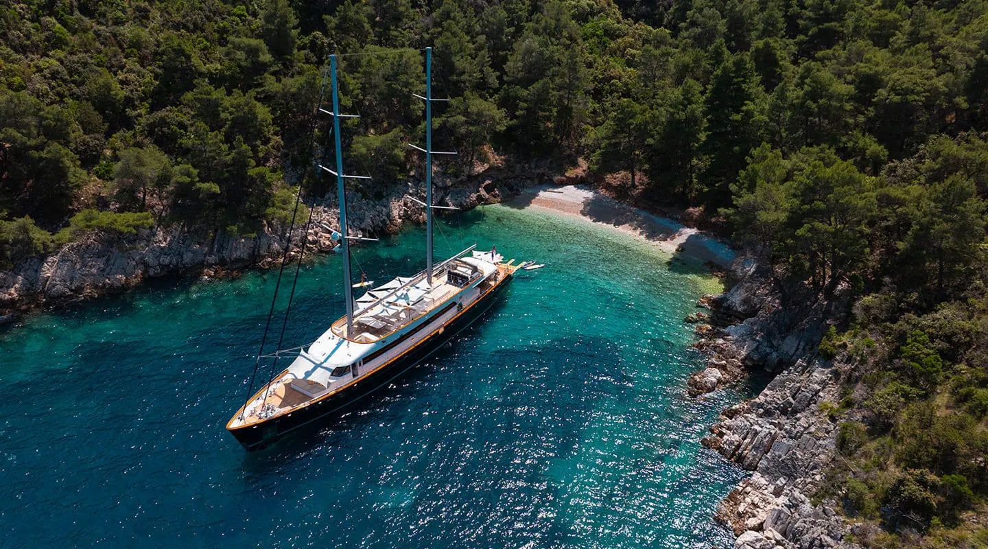 Two-masted motor yacht anchored in turquoise water near rocky coastline