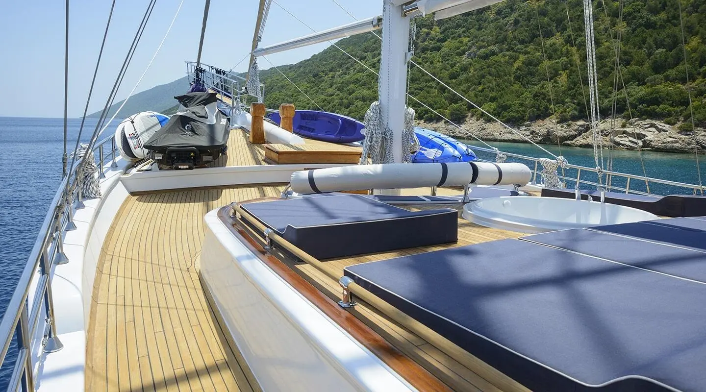 Bella Mare yacht deck with blue sun loungers, wooden railing, and calm marina view