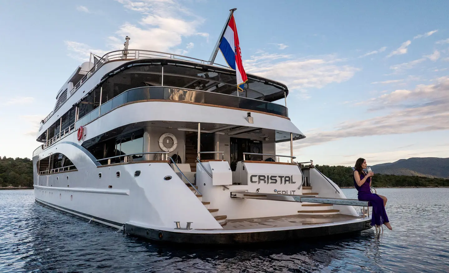 Cristal yacht moored with white hull, flag on top, dusk sky reflected