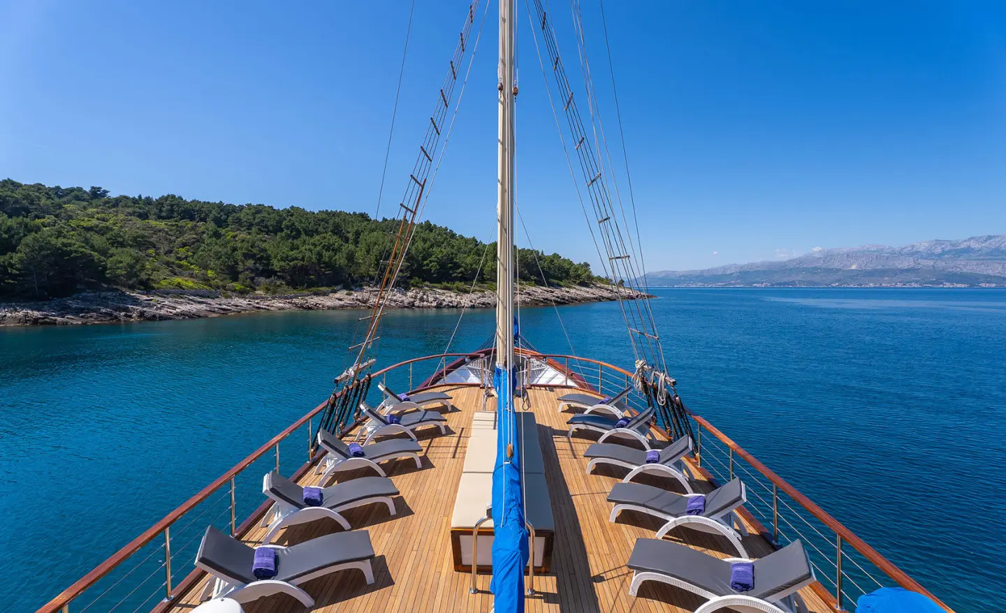 View along the wooden deck toward the bow of Mendula yacht at sea during calm blue hour