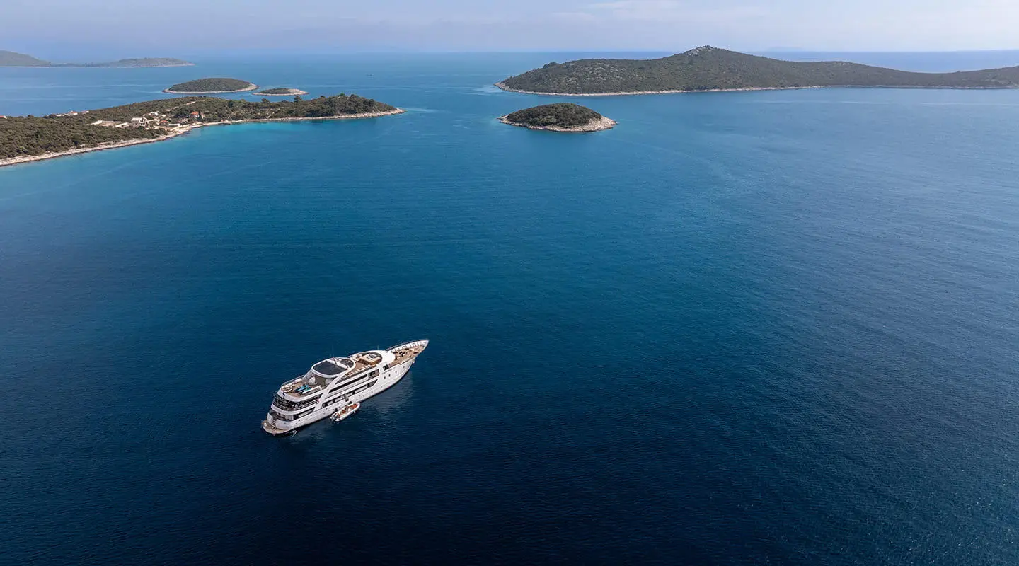 A sleek luxury yacht named Karizma anchored in blue sea near small islands