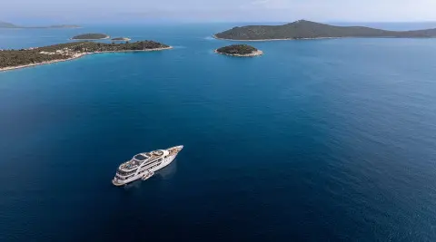A sleek luxury yacht named Karizma anchored in blue sea near small islands
