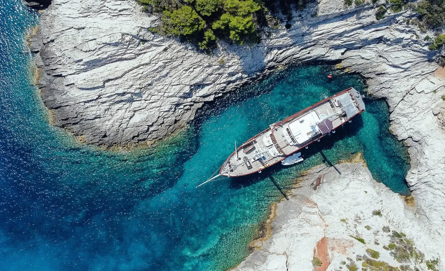 Luxurious gulet yacht anchored in turquoise blue water among rocky coast