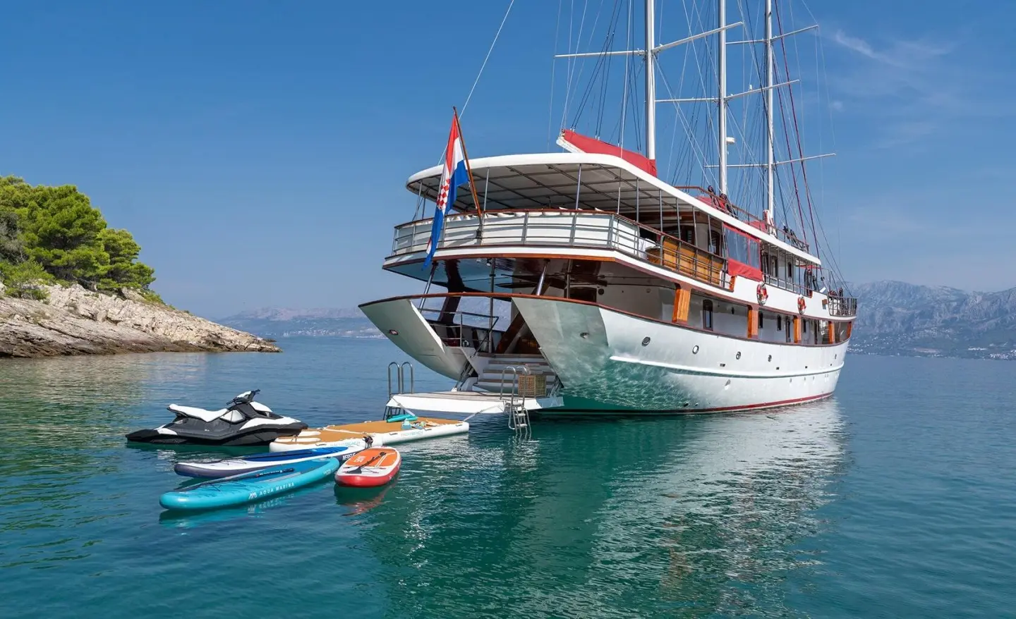 Large motor yacht moored in clear blue water with small watercraft nearby
