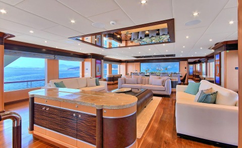 Luxurious yacht interior with white sofas and a curved marble bar, facing an ocean view