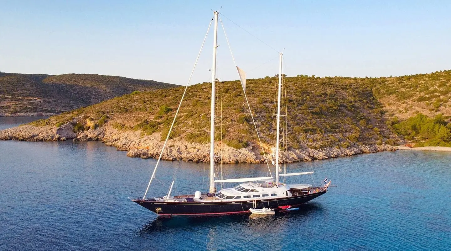Yacht Tamarita anchored in blue sea with hilly coastline in background