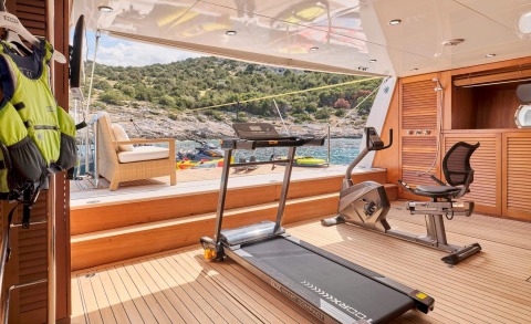 On the Mobius yacht, a treadmill and exercise bike on a wooden deck with an outdoor seating area and water view