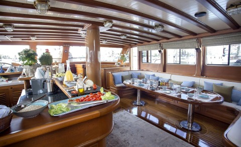 Wooden yacht interior with dining table and open galley area in saloon