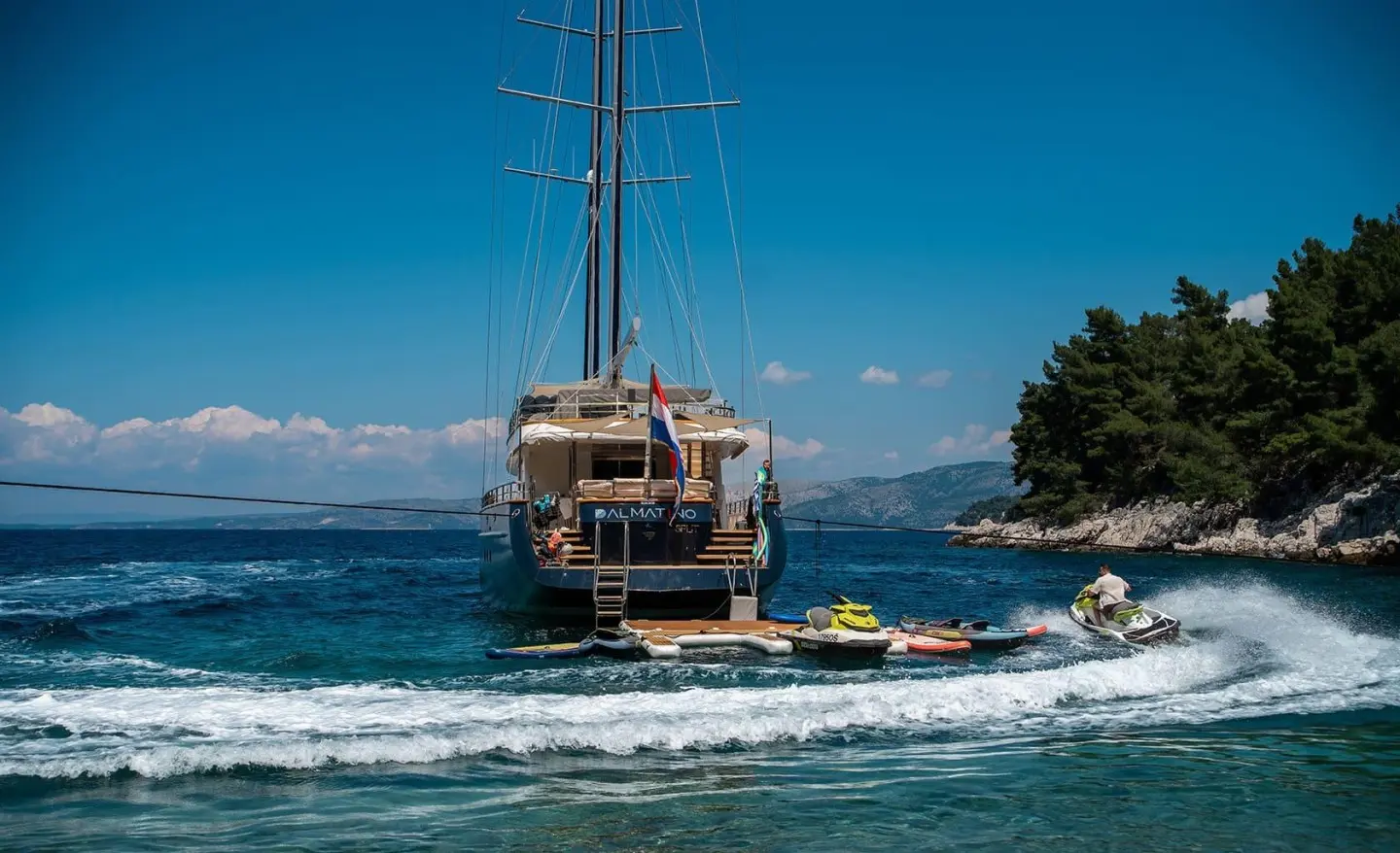 Dalmatino yacht anchored near rocky coast with clear blue water