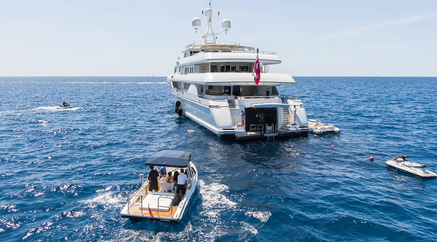 Apogee yacht anchored near a small tender with guests aboard, clear blue sea