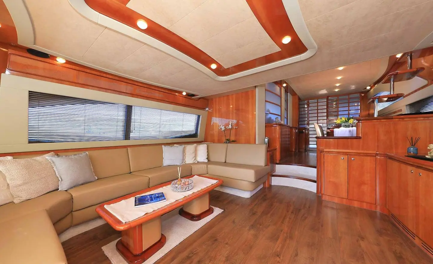 Interior of luxury yacht salon with beige seating, wooden deck, and a coffee table