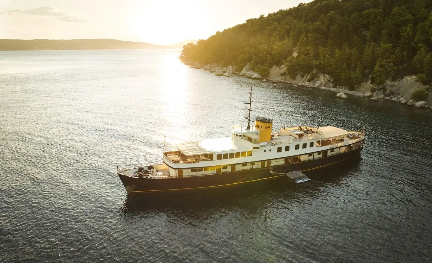 Seagull II yacht anchored near rocky coastline at sunset, calm water