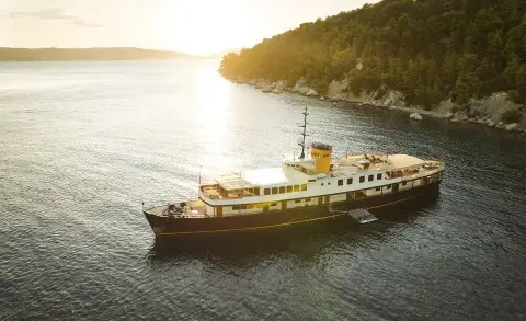 Seagull II yacht anchored near rocky coastline at sunset, calm water