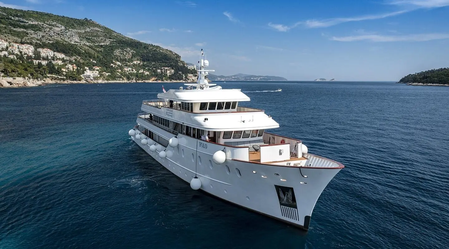 Yolo luxury yacht anchored in blue sea with mountain coastline in background