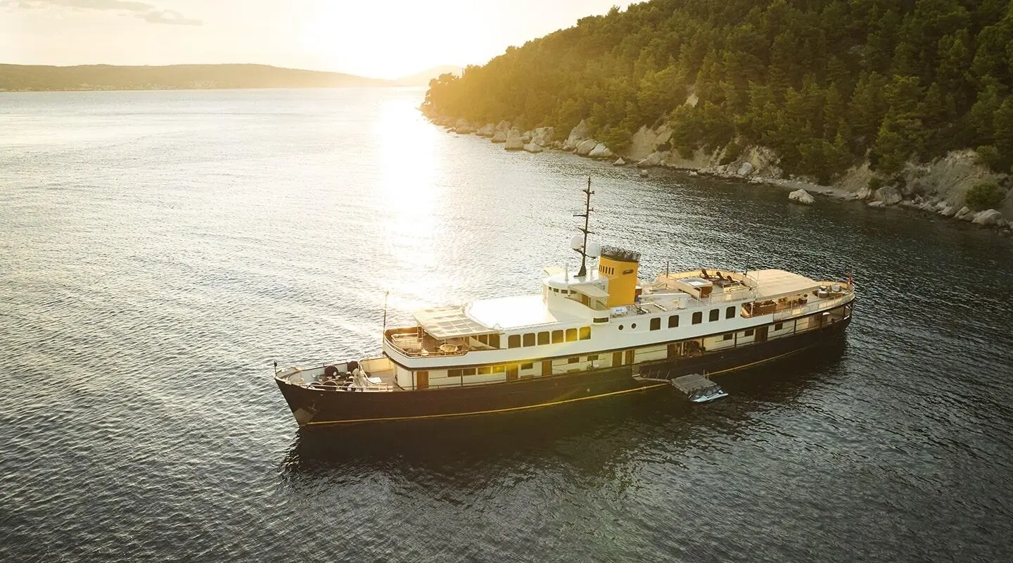 Seagull II yacht anchored near rocky coast at sunset, calm water
