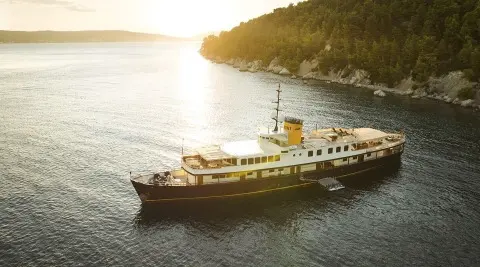 Seagull II yacht anchored near rocky coast at sunset, calm water