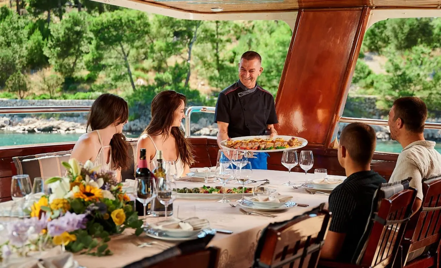 Luna motor yacht dining on deck with guests and waiter under shaded canopy