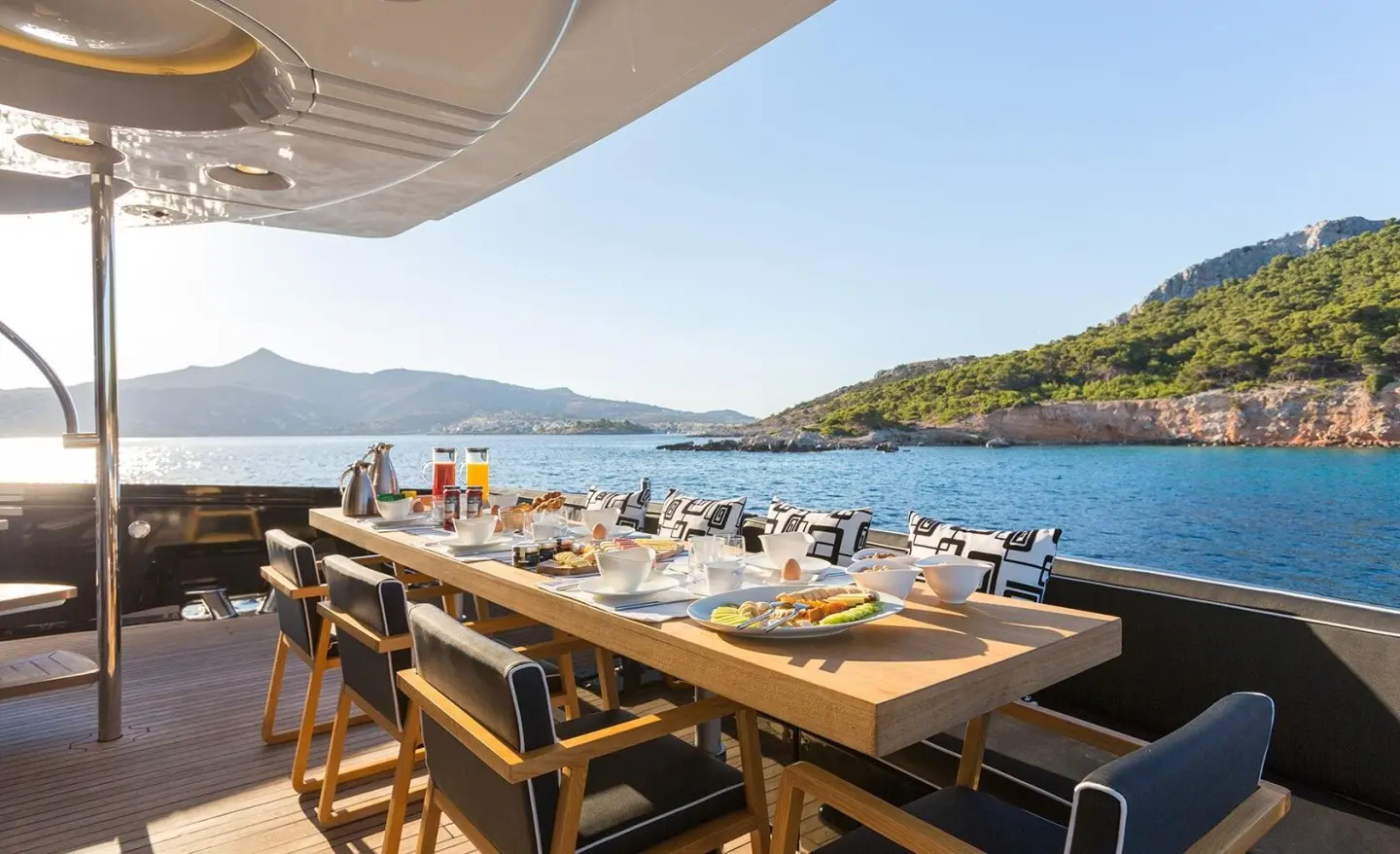 Aquarella yacht dining setup on deck with long wooden table and seaside view