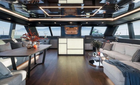 Alteya yacht interior: modern lounge with L-shaped sofa, glass-top table, and a central illuminated bar area