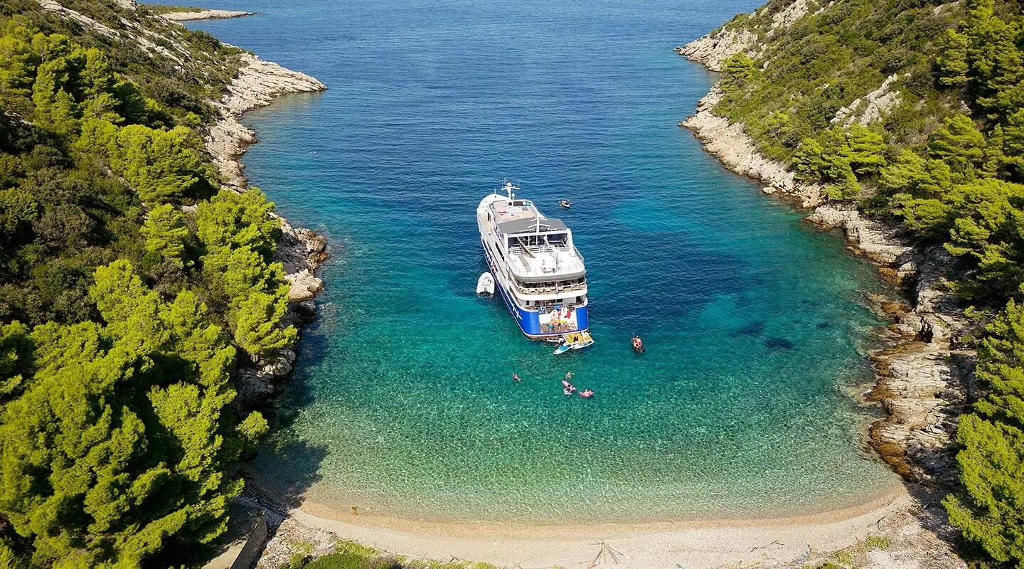 Motor yacht Lupus Mare anchored in a clear turquoise cove with surrounding green cliffs