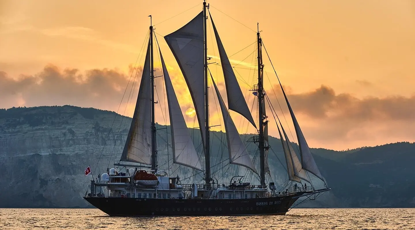 Gulet yacht named Running on Waves sailing at sunset with tall sails
