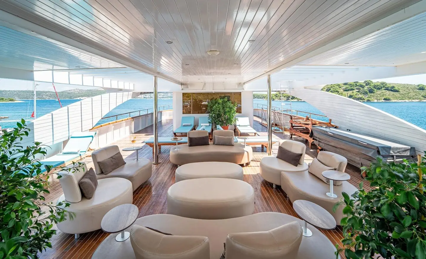 Sunlit yacht sundeck with curved beige seating, glass railing, ocean view