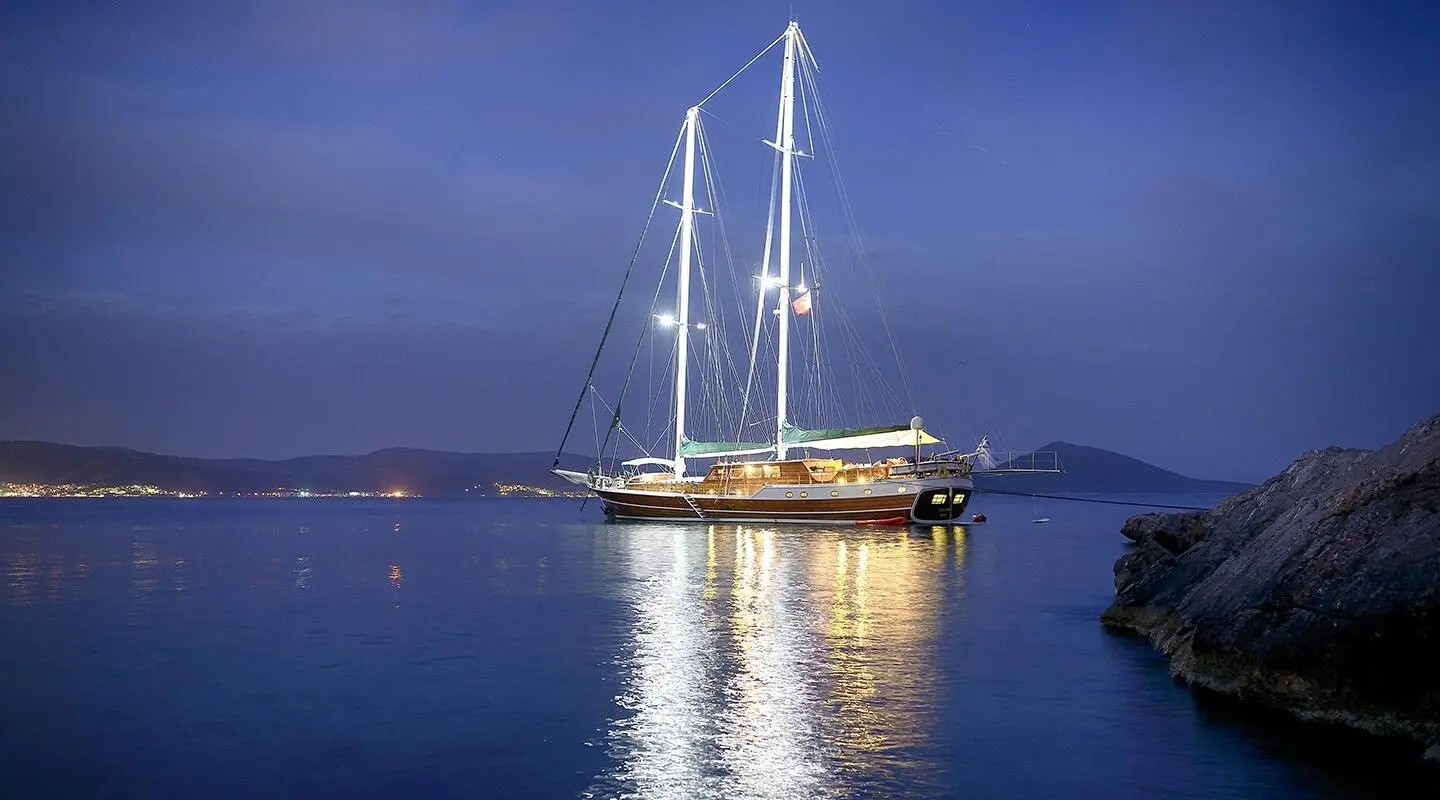 Gulet Ecce Navigo at night, illuminated hulls reflecting on calm waters
