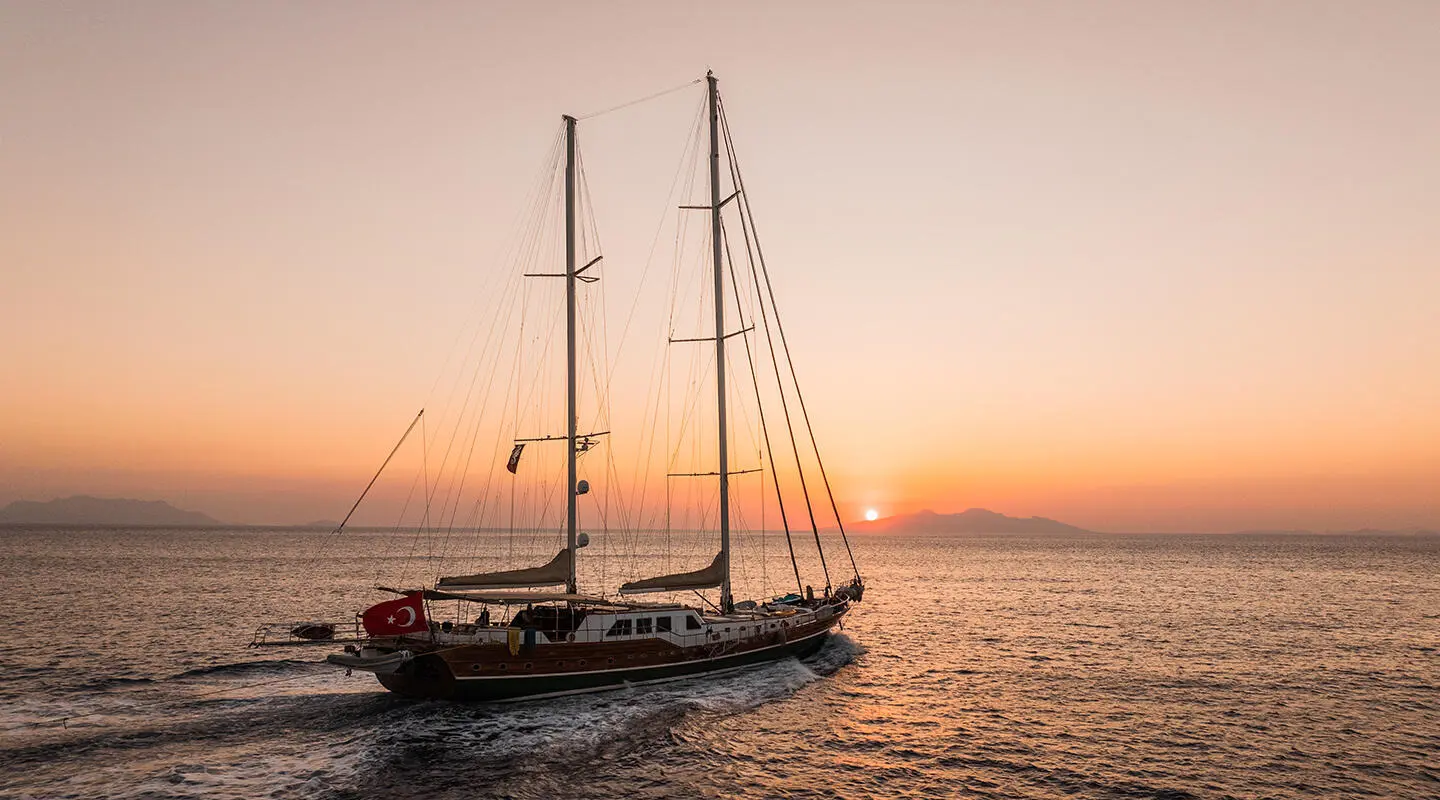 Sunset over calm sea with a two-masted luxury gulet yacht at anchor