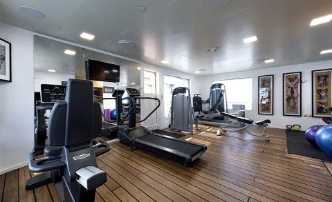 Interior of Chakra yacht gym with treadmills, ellipticals, and fitness equipment on polished wood deck