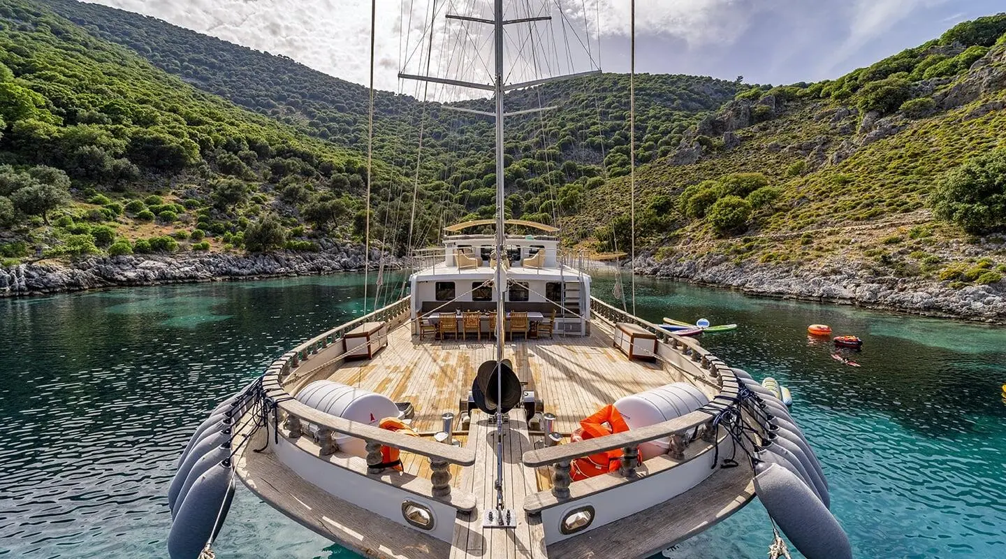 Yacht Tersane 8 seen from bow, polished wood deck, sails furled, sunset glow