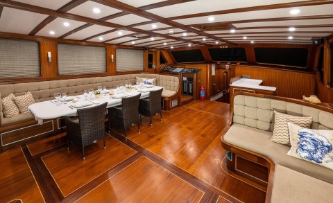 Interior of Estrella De Mar luxury yacht with wood paneling, long dining table set with plates and glasses, beige upholstered seating and cushions