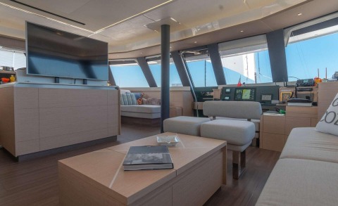 Interior of Serenissima with seating area and helm panel, large TV visible beyond the coffee table.
