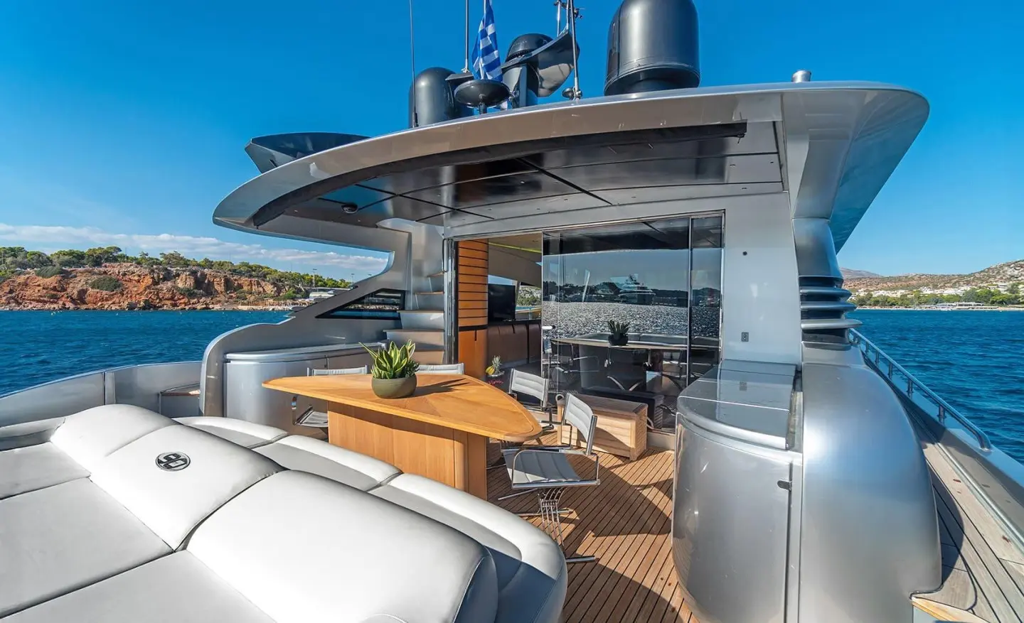 Luxury yacht deck with wooden table and seating, sea and coastline view