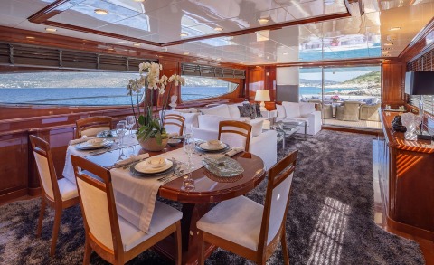 Divine luxury yacht dining area with wooden interior, long table set for six, ocean view windows