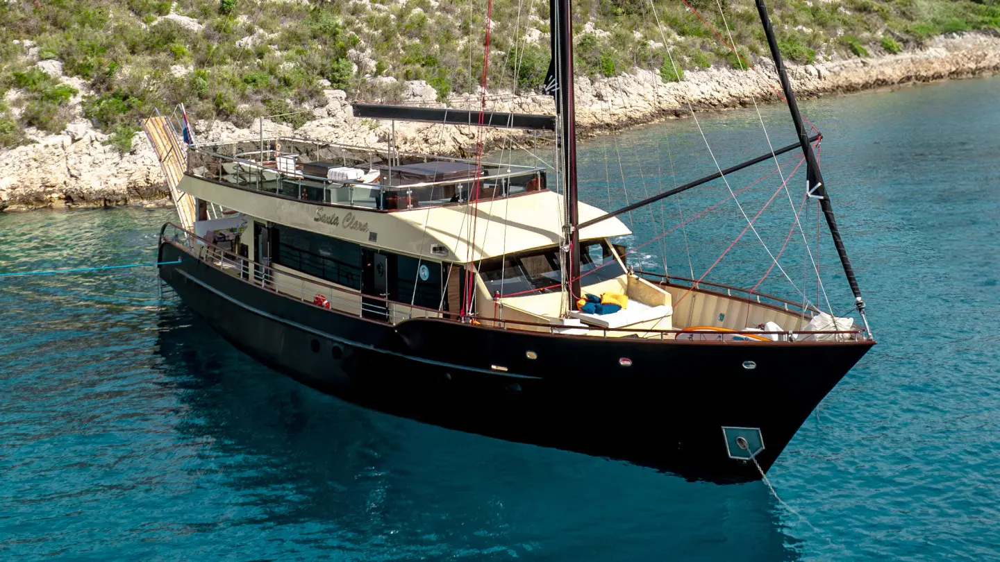 Yacht Santa Clara anchored near rocky shore with azure water and deck details