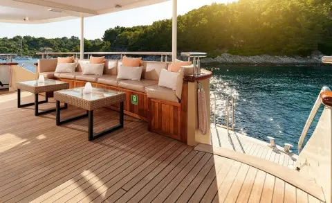 Queen Eleganza yacht deck at sunset with seating, wooden railing, and water views