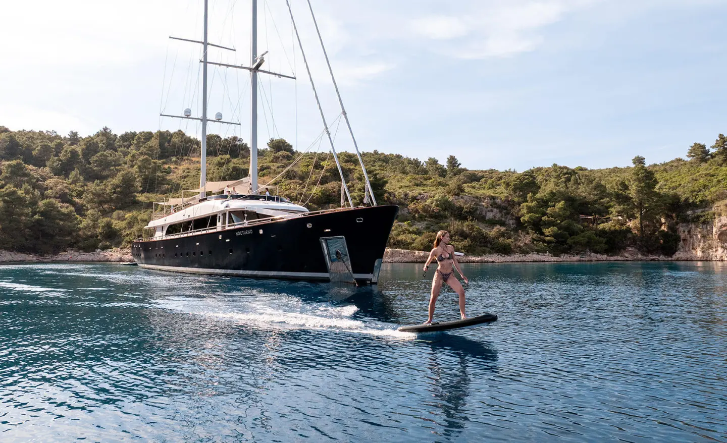 Nocturno luxury yacht anchored near shore with a person paddleboarding nearby