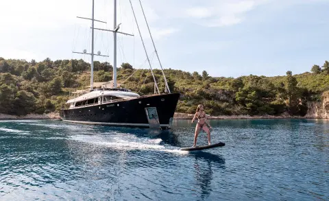 Nocturno luxury yacht anchored near shore with a person paddleboarding nearby
