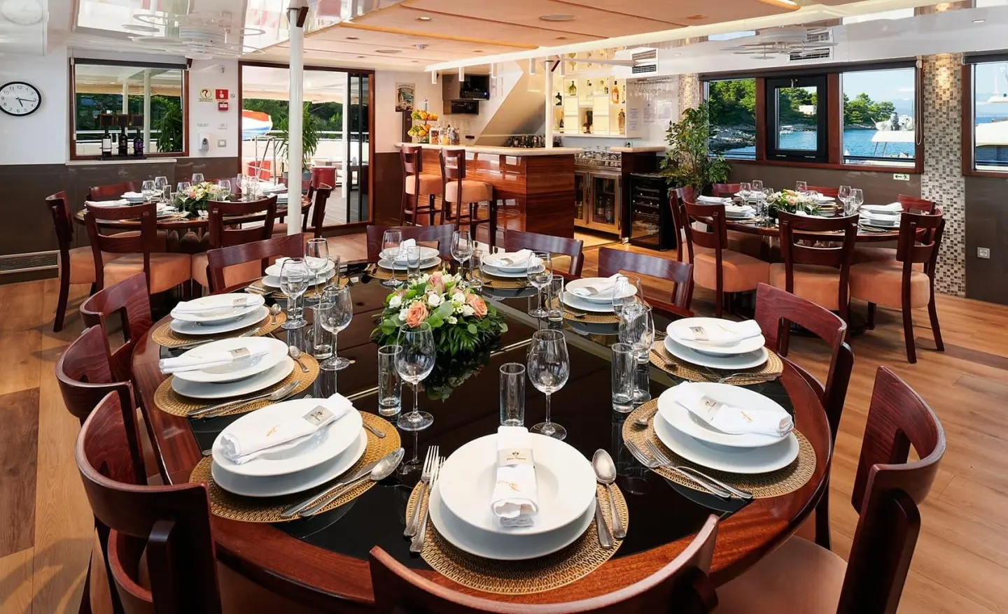 Queen Eleganza yacht dining table set with plates, glassware at sunset