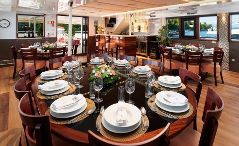 Queen Eleganza dining area aboard luxury yacht, round table set for eight with flowers