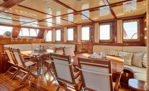 Interior of Myra yacht dining area with wood paneling, large windows, and cream cushions
