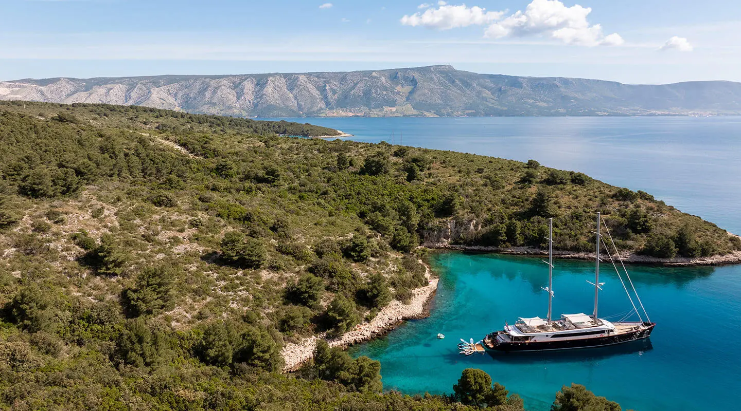 Nocturno yacht anchored near rocky coastline with clear blue water