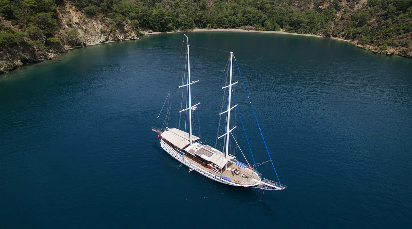 Kayhan 5 yacht anchored in blue water with two masts near rocky coastline
