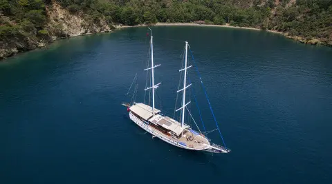 Kayhan 5 yacht anchored in blue water with two masts near rocky coastline